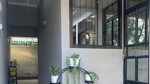 A hallway with a potted plant stand, a window with decorative grills, and a door with a black frame. - Ilboru Haven Homes (Arusha)