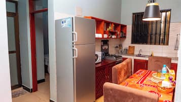 Una cocina compacta con refrigerador, microondas y estufa, una mesa de comedor con mantel, y una lámpara colgante.