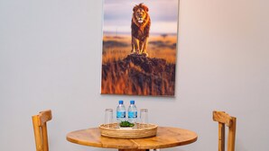 A round wooden table with two wooden chairs, a woven placemat, a framed picture of a lion, and two bottles of water. - Ilboru Haven Homes (Arusha)
