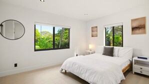 A bedroom with a large bed, two bedside tables, a nightstand, a round mirror, and two windows with a view of greenery. - Superb Miami 4 Bedrooms, 3 Bath home, Perfect for Families & Groups (Miami)