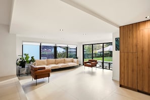 Ein modernes Wohnzimmer mit einer Couch, Sesseln, einem Holzschrank und großen Fenstern.