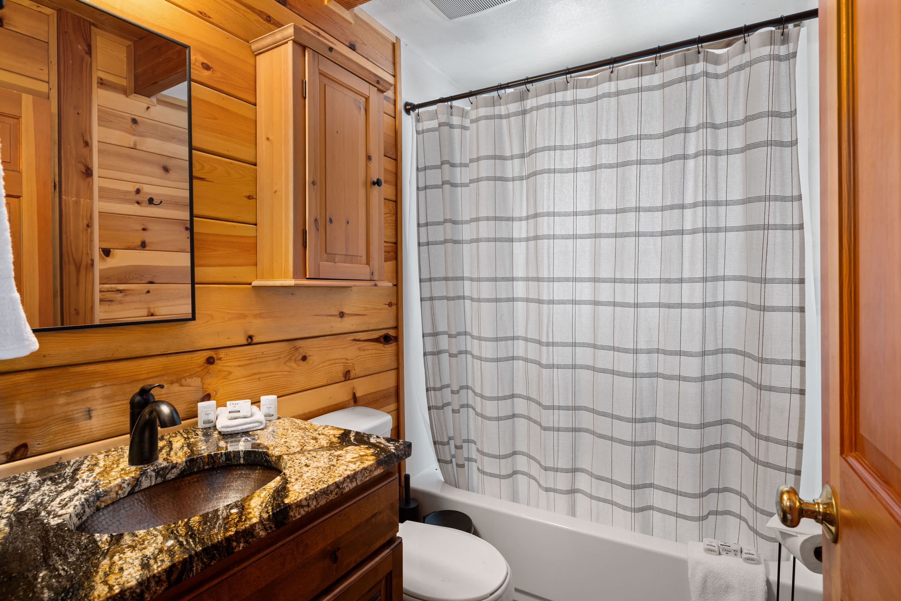 Une salle de bain avec un meuble-lavabo en bois, un évier, des toilettes et un rideau de douche.