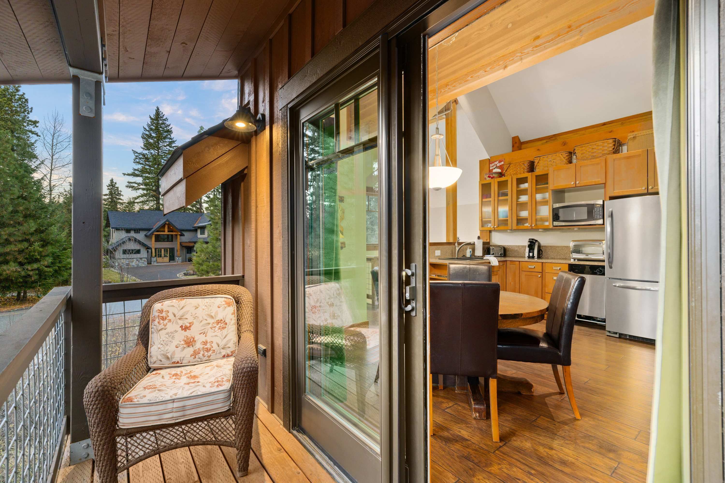 Un balcon agrémenté de meubles en osier, une porte-fenêtre coulissante donnant sur une cuisine avec des meubles en bois et des appareils électroménagers modernes.