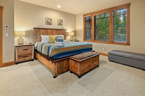 Ein Schlafzimmer mit einem großen Bett, einem Holz-Kopfende, zwei Nachttischen, einer Bank und einem Fenster mit Jalousien.