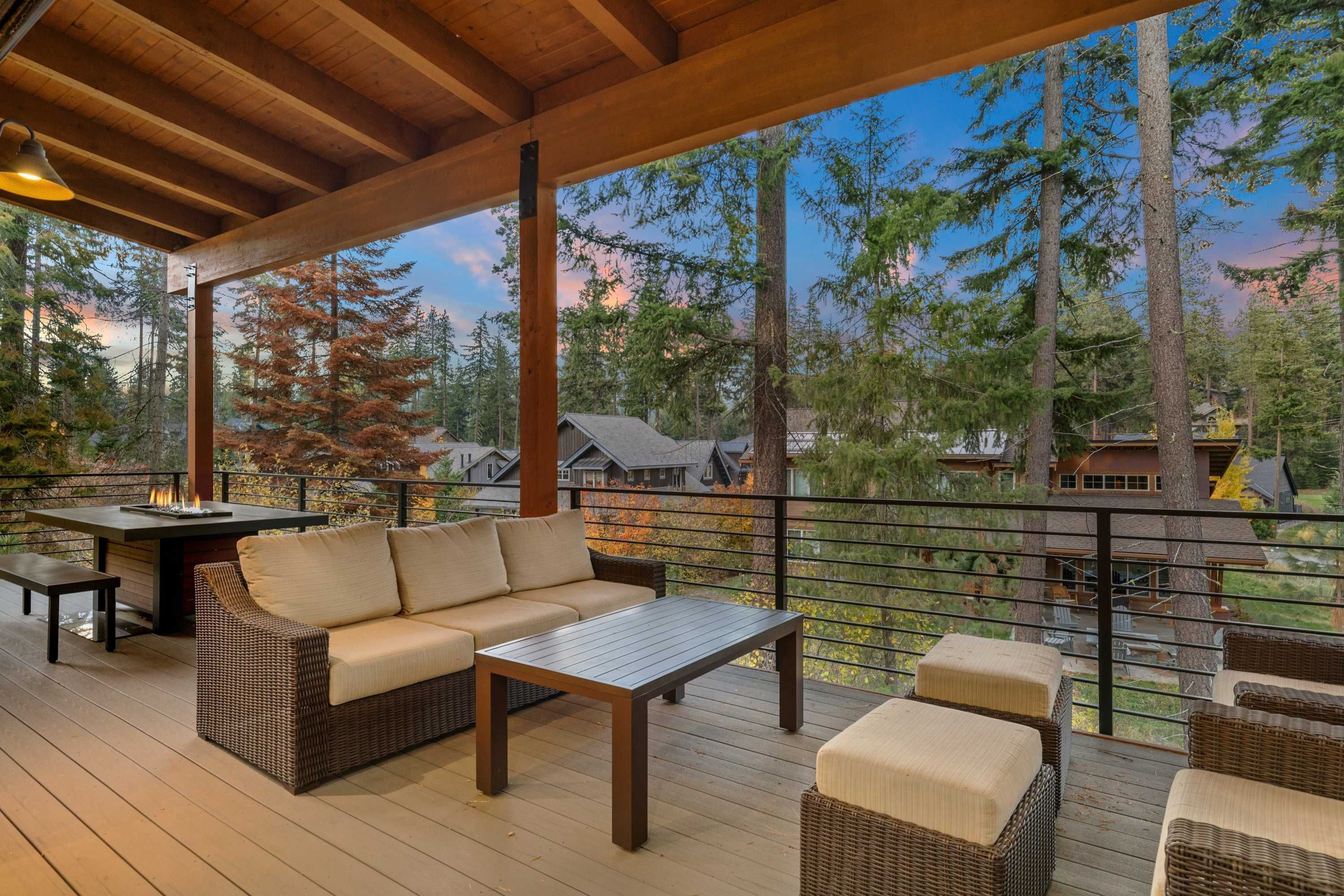Eine überdachte Terrasse mit einer Couch, einem Tisch und Stühlen mit Blick auf eine bewaldete Landschaft.