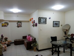 Ein Wohnzimmer mit einer Couch, einem Esstisch mit Glasplatte und einem kleinen Beistelltisch mit einer Vase.