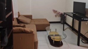 Un salon avec un canapé, une petite table, un téléviseur et un luminaire au plafond.