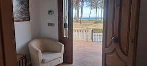 Une porte ouverte donnant sur un balcon avec vue sur la plage et les palmiers.