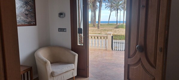 Een open deur die uitkomt op een balkon met uitzicht op het strand en palmbomen.