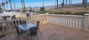 Een terras buiten met tafels en stoelen, een leuning en uitzicht op het strand en de oceaan.