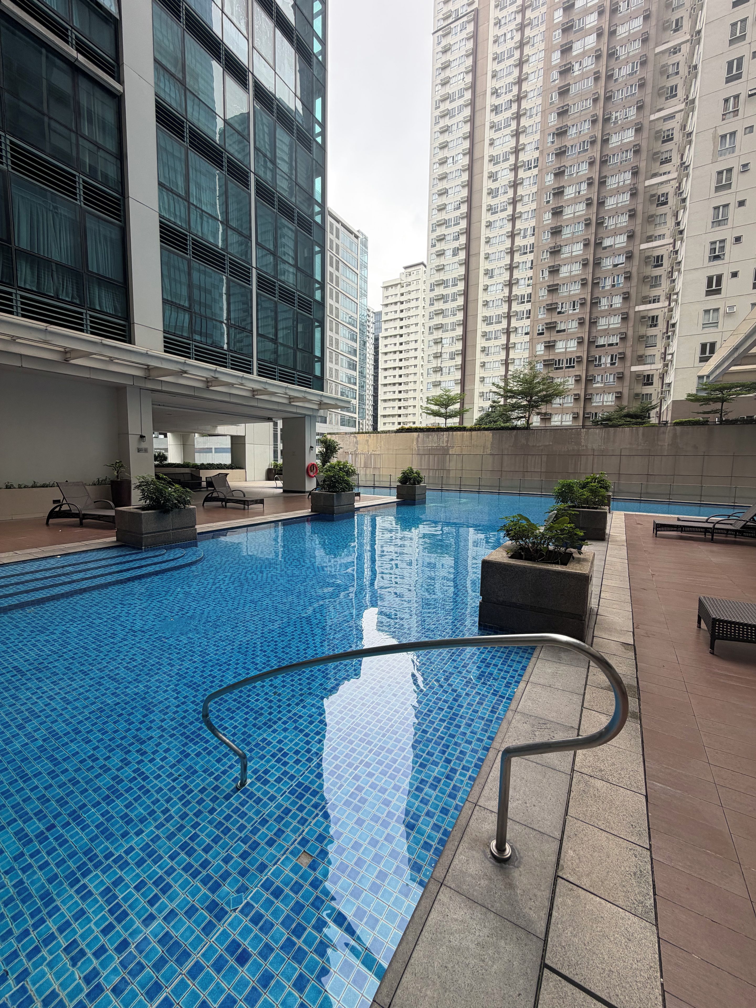 A swimming pool with a tiled deck, surrounded by high-rise buildings.