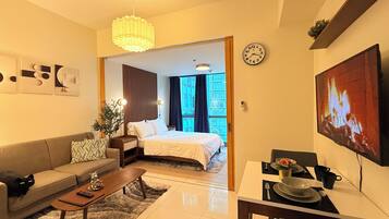 A modern hotel room with a sofa, a dining table, a bed, a TV, and a large window.