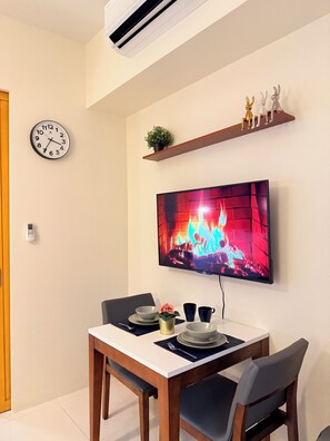 Ein Essbereich mit Fernseher, der einen Kamin zeigt, einer Uhr und einem Regal mit Dekoration.