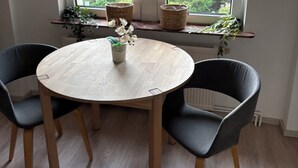 Ett runt träbord med två stolar, ett fönster med utsikt över grönskan och en hylla med växter.