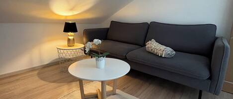 Een moderne woonkamer met een grijze bank, een ronde witte salontafel en een vloerlamp.