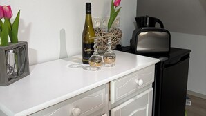 Ett litet kök med en vit bänkskiva, en vinflaska, två glas, en brödrost och ett svart kylskåp.