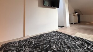 Ett sovrum med en säng, en tv som är monterad på väggen och ett litet kök i bakgrunden.