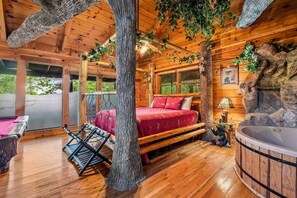 Ein Holzblockhaus-Interieur mit einem Bett, einer Whirlpool-Badewanne und Blick auf die Natur.