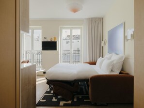 Ein Hotelzimmer mit Bett, Fernseher, Balkon und Blick auf Gebäude.