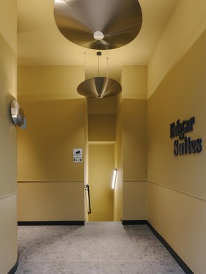 A hallway with a sign for 'Eloan Suites,' a ceiling fan, and a wall-mounted light fixture. - Edgar Suites - Jules Ferry (Paris)
