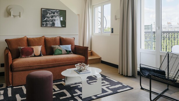 A modern living room with a brown sofa, a white coffee table, a patterned rug, and a balcony with a view. - Edgar Suites - Jules Ferry (Paris)