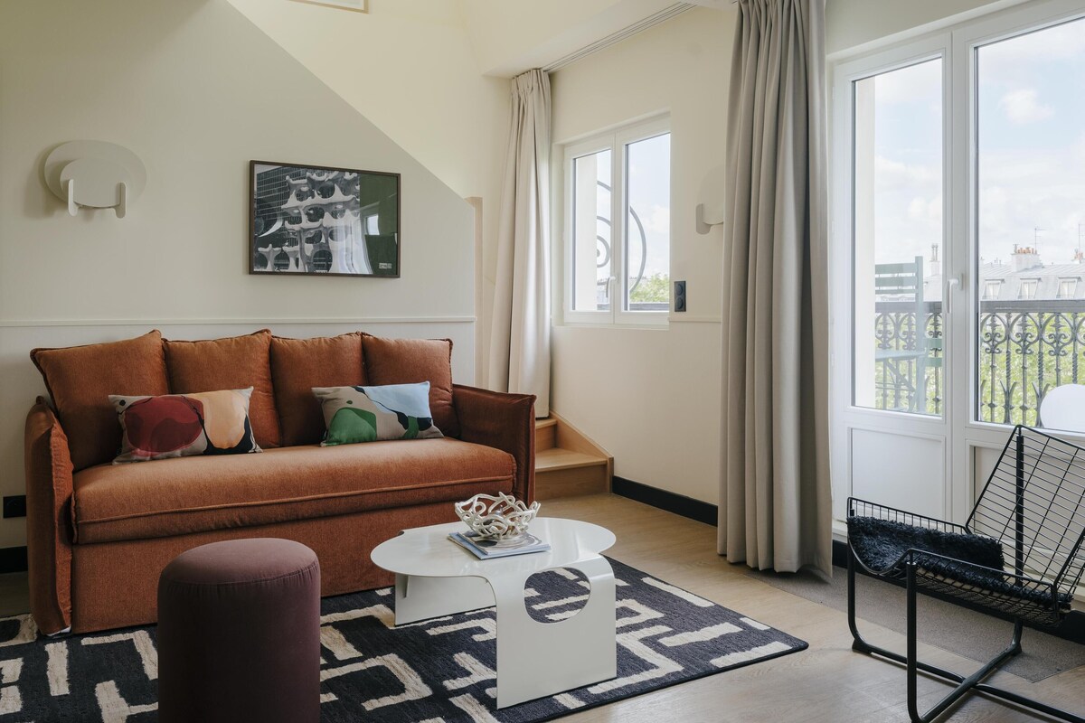 Ein modernes Wohnzimmer mit einem braunen Sofa, einem weißen Couchtisch, einem gemusterten Teppich und einem Balkon mit Blick.