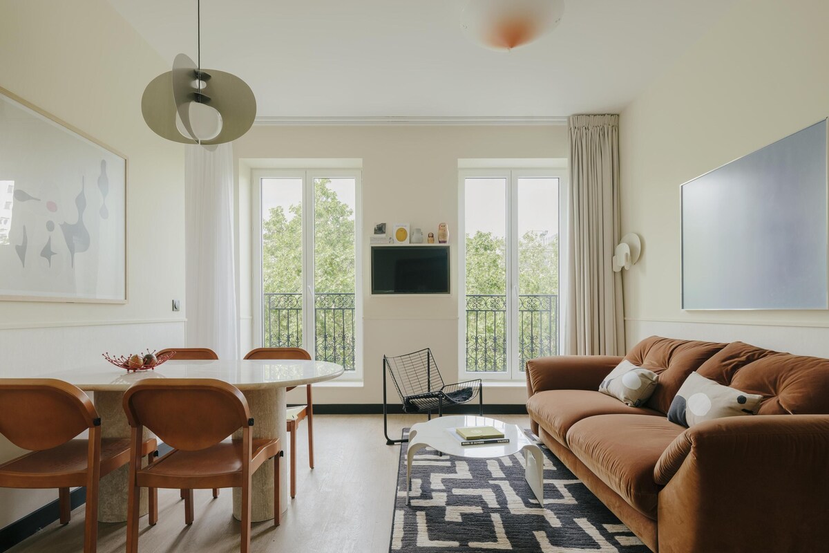 Ein modernes Wohnzimmer mit einem runden Esstisch, einer braunen Ledersofa und einem großen abstrakten Gemälde.