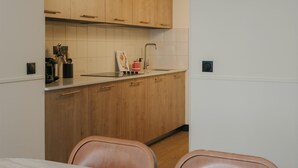 A modern kitchen with wooden cabinets, a white countertop, and a dining area with a table and chairs. - Edgar Suites - Jules Ferry (Paris)