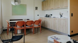 A modern kitchen with wooden cabinets, a dining area with orange chairs, and a black chair with a mesh backrest. - Edgar Suites - Jules Ferry (Paris)