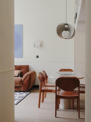 A modern dining area with a round table, wooden chairs, and a pendant light. - Edgar Suites - Jules Ferry (Paris)