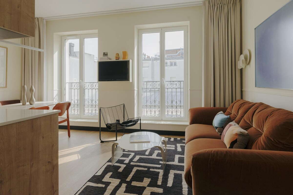 Ein modernes Wohnzimmer mit einer Couch, einem Couchtisch, einem an der Wand montierten Fernseher und einem Balkon mit Geländer.