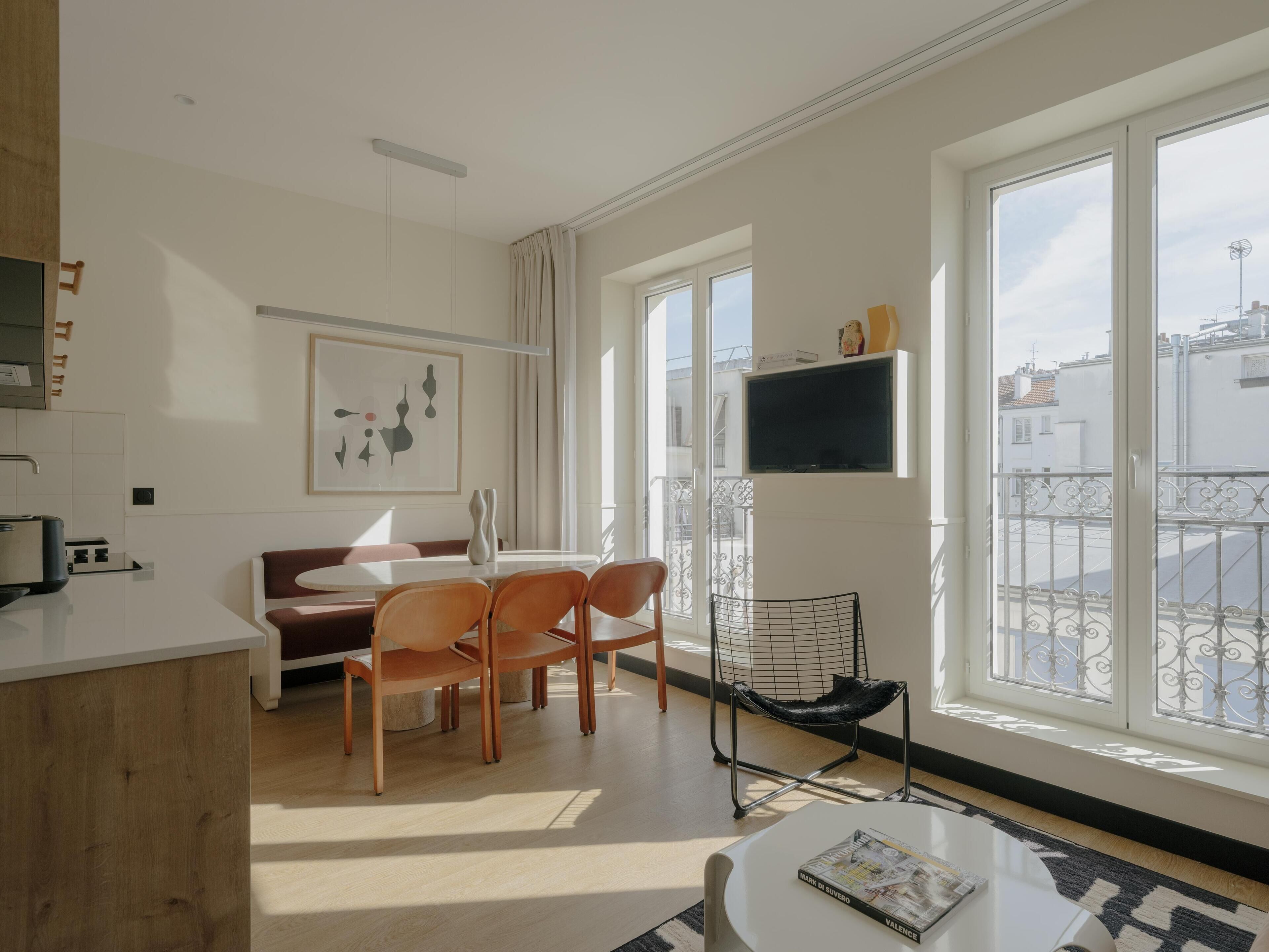A modern living room with a dining area, large windows, a flat-screen TV, and a balcony.