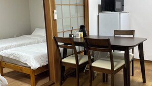 Quarto com cama, mesa, cadeiras, micro-ondas e geladeira.