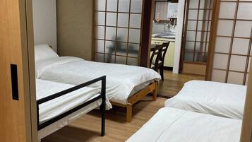 A hotel room with two beds, a wooden floor, a sliding door, and a kitchenette in the background.