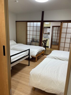 Une chambre dâhĂŽtel avec deux lits, un plancher en bois, une porte coulissante et, au fond, une petite cuisine.