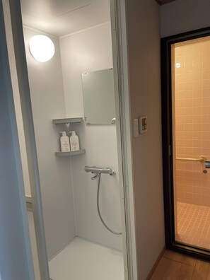 A shower with a handheld showerhead, a wall-mounted mirror, and a shelf with toiletries.