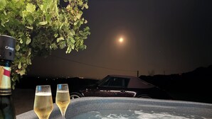 Ein Whirlpool mit zwei Weingläsern und einer Flasche, unter einem Sternenhimmel mit Mond.