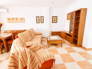 A living room with a striped sofa, a wooden coffee table, a dining table with chairs, and a wooden cabinet. - Apartamento San Jose bajo (Conil de la Frontera)