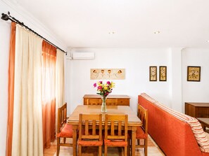 Een eetgedeelte met een tafel, stoelen, een bloevas, een bank en wanddecoratie.
