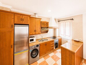 A kitchen with wooden cabinets, a stainless steel refrigerator, a microwave, a sink, a stove, and a washing machine. - Apartamento San Jose bajo (Conil de la Frontera)