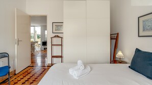 Habitación de hotel con cama, una silla, una escalera de madera, una mesa con lámpara y un cuadro en la pared.