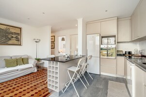 Una cocina moderna con una isla central, muebles blancos y un comedor con sillas.