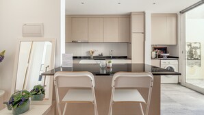 Una cocina moderna con una isla central, sillas blancas, una lavadora y un ventanal grande.
