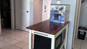 Een kitchenette met een magnetron, koffiezetapparaat en een afvalbak.