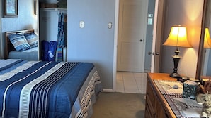 Een slaapkamer met een bed, een dressoir, een plafondventilator, een deur en een lamp.