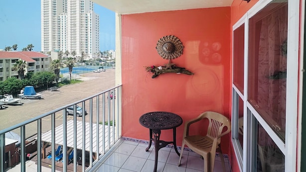 Een balkon met een betegelde vloer, een klein rond tafeltje, een plastic stoel en een decoratief object aan de muur.