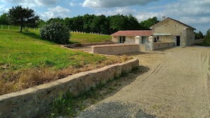 A rural property with a stone building, a gravel driveway, and a fenced area.