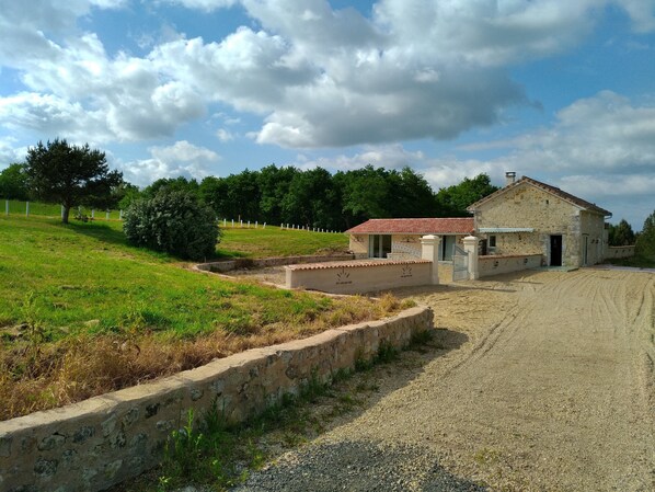 A rural property with a stone building, a gravel driveway, and a fenced area.