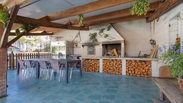 Un patio al aire libre con una chimenea de ladrillo, una mesa de comedor con sillas y una estructura de pérgola de madera.