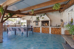 An outdoor patio with a brick fireplace, a dining table with chairs, and a wooden pergola structure.